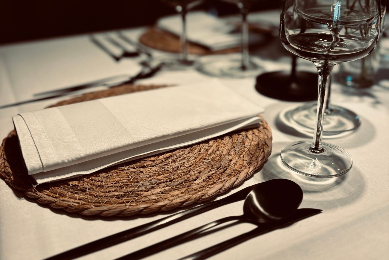 Tischgedeck mit Tellern, Besteck und gefalteter Serviette auf einem eleganten Tisch.