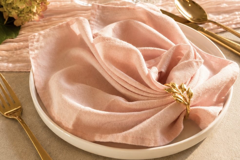 Tischgedeck mit Tellern, Besteck und gefalteter Serviette auf einem eleganten Tisch.